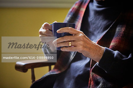 Senior woman sitting in chair, holding hot drink, mid section
