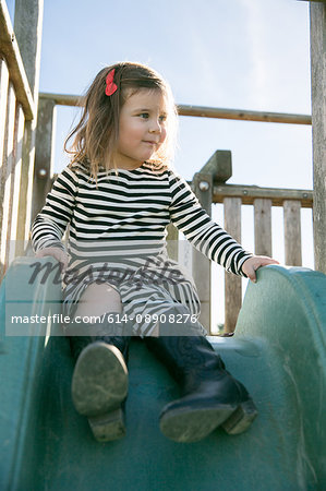 Cute girl in striped dress sitting on playground slide