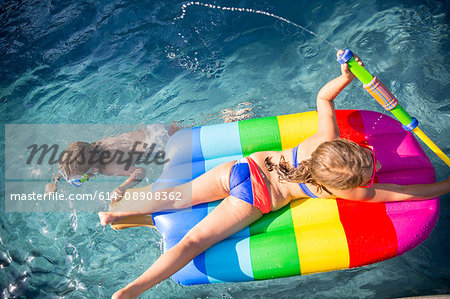 Overhead view of boy swimming and girl on inflatable in outdoor swimming pool