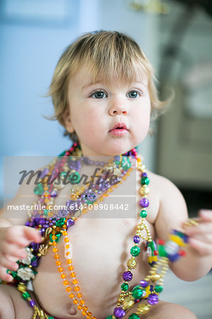 Female toddler trying on bead necklaces in kitchen