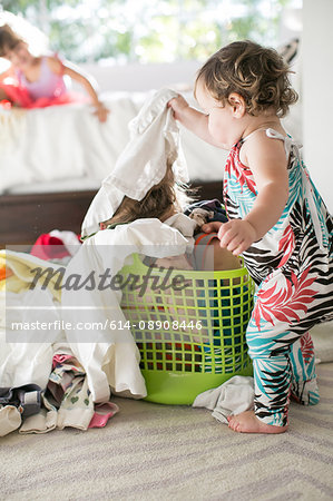 Female toddler removing laundry from child hiding in laundry basket