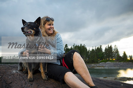 Senior woman sitting on rock hugging dog at coast of Maine, USA
