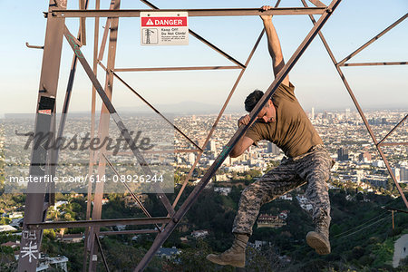 Soldier wearing combat clothing dangling from electricity pylon, Runyon Canyon, Los Angeles, California, USA