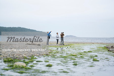 Father and sons taking photographs on beach, Pacific Rim National Park, Vancouver Island, Canada
