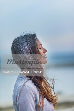 Profile of mature woman outdoors, eyes closed, wind blowing hair
