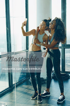 Two young women in gym, taking selfie, using smartphone