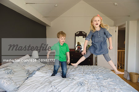 Girl and brother jumping on bed together