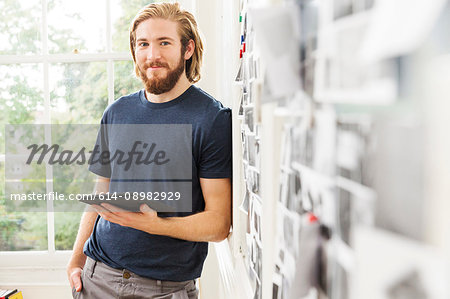 Portrait of young male designer leaning against mood board in creative studio Portrait of young male designer leaning against mood board in creative studio