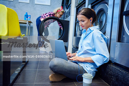 Woman sitting on laundrette floor typing on laptop