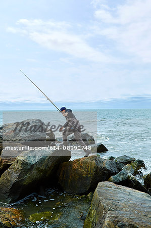 Young male sea fisher stepping over beach rocks