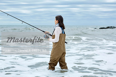 Young woman in waders sea fishing knee deep in water