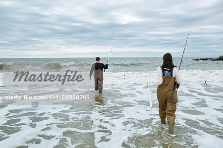 Young sea fishing couple in waders, wading in sea