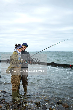 Young man ankle deep in water teaching girlfriend sea fishing