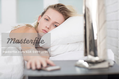 Young woman in bed, reaching for smartphone on bedside table