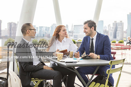 Businessmen and woman meeting at waterfront cafe with New York skyline, USA