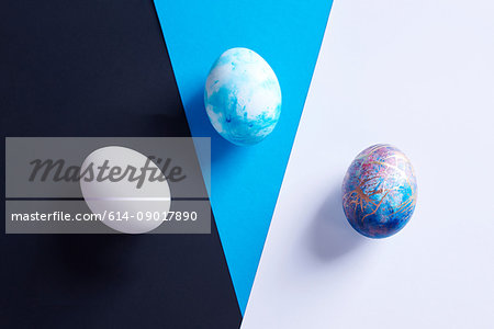 Overhead view of three dyed easter eggs on blue, black and white shapes