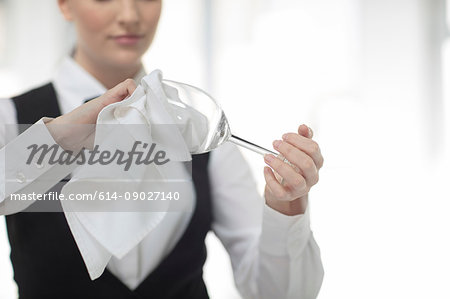 Waitress polishing wine glass in restaurant, mid section