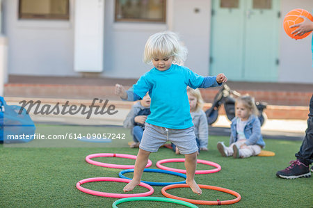 Girl at preschool, jumping above plastic hoops in garden