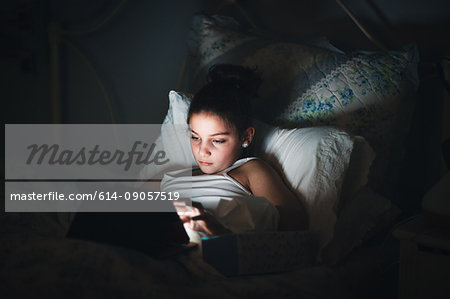 Girl in bed illuminated by light from digital tablet