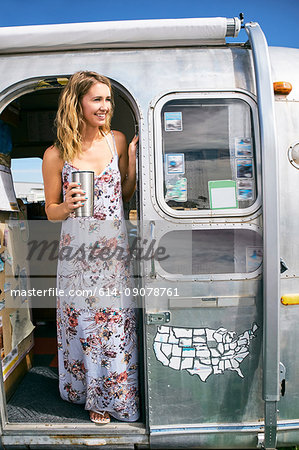 Young woman wearing maxi dress looking out from airstream doorway