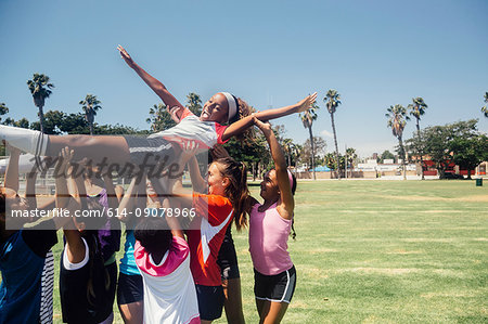 Schoolgirl soccer team carrying player above their heads on school sports field
