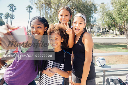 Schoolgirl soccer players taking smartphone selfie on school sports field