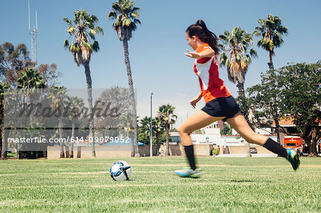 Teenage schoolgirl running to kick soccer ball on school sports field