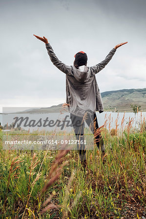 Young woman standing near Dillon Reservoir, arms raised, rear view, Silverthorne, Colorado, USA