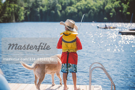Rear view of dog and boy in cowboy hat fishing from lake pier