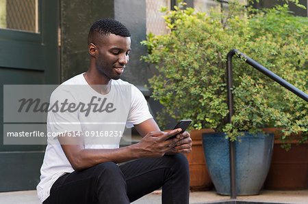 Young man using cellphone on step in streets of New York, US