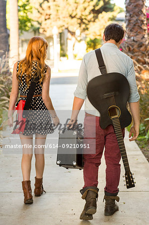 Young couple walking along street carrying guitars and amplifier