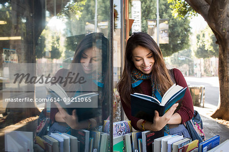 Young woman reading book by shop window