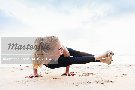 Mid adult woman poised in yoga position on beach