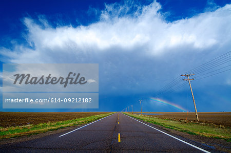 A highway leads to a storm and a rainbow west of Healy, Kansas, USA