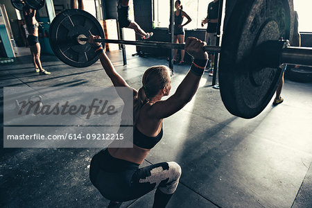 Rear view of female crossfitter crouching with barbell in gym