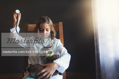 Girl sitting on chair dressed up as doctor tending to Boston terrier puppy using stethoscope