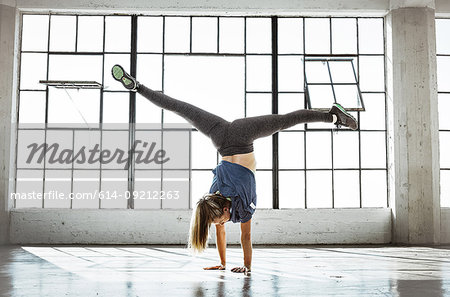 Rear view of young woman in gym doing handstand, open legs