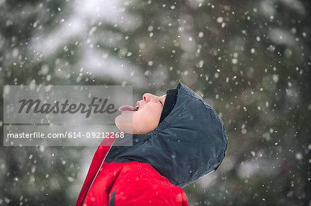 Side view of boy sticking out tongue catching snowflakes