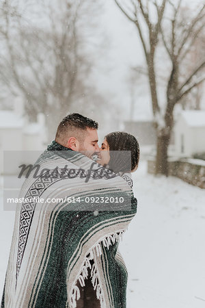 Couple wrapped in blanket kissing in snowy landscape, Georgetown, Canada