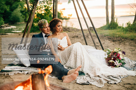 Bride and groom on picnic blanket by lakeside campfire, Lake Ontario, Toronto, Canada