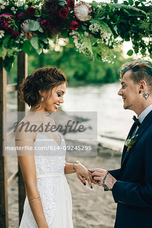 Groom putting on bride's ring on lakeside
