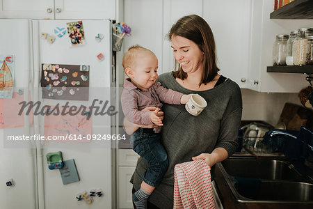 https://image1.masterfile.com/getImage/614-09249664em-mother-carrying-baby-son-drying-dishes-in-kitchen-stock-photo.jpg