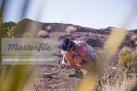 Man squatting in desert looking at control panel for drone (unmanned aerial vehicle)