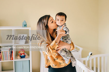 Mother kissing baby son in nursery, portrait