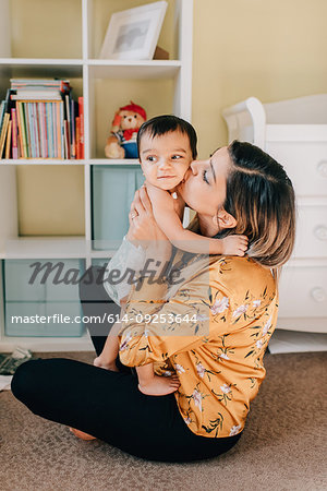 Mother sitting on nursery floor kissing baby son
