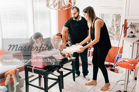 Mid adult couple in kitchen with daughter and baby son in high chairs