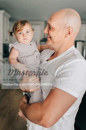 Father carrying baby daughter in living room, portrait