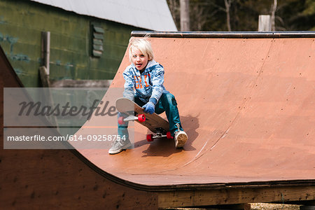 Boy preparing to sit down on skateboard on wooden skateboard ramp