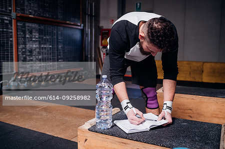 Young man reading checklist on notebook in gym