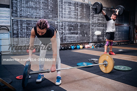 Young woman placing weight plate into bar in gym